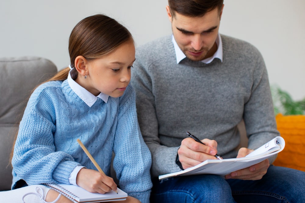 Padre ayudando a su hija a hacer deberes escolares. Freepik